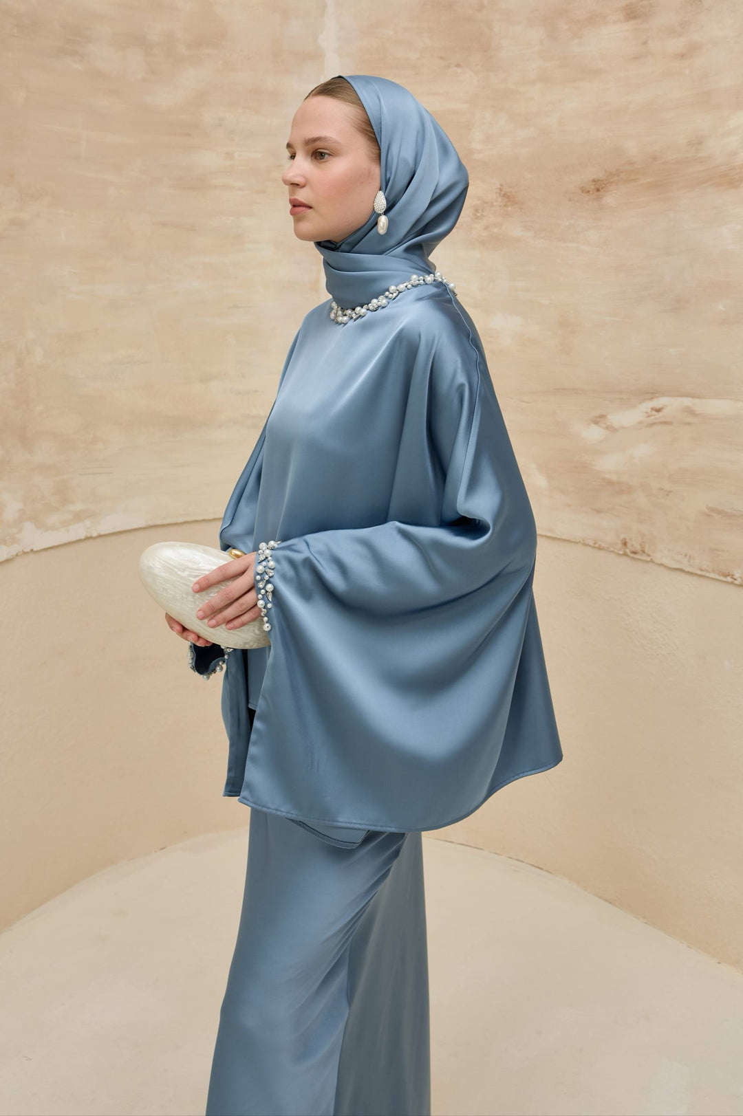 Woman in a blue outfit with a matching headscarf against a beige background