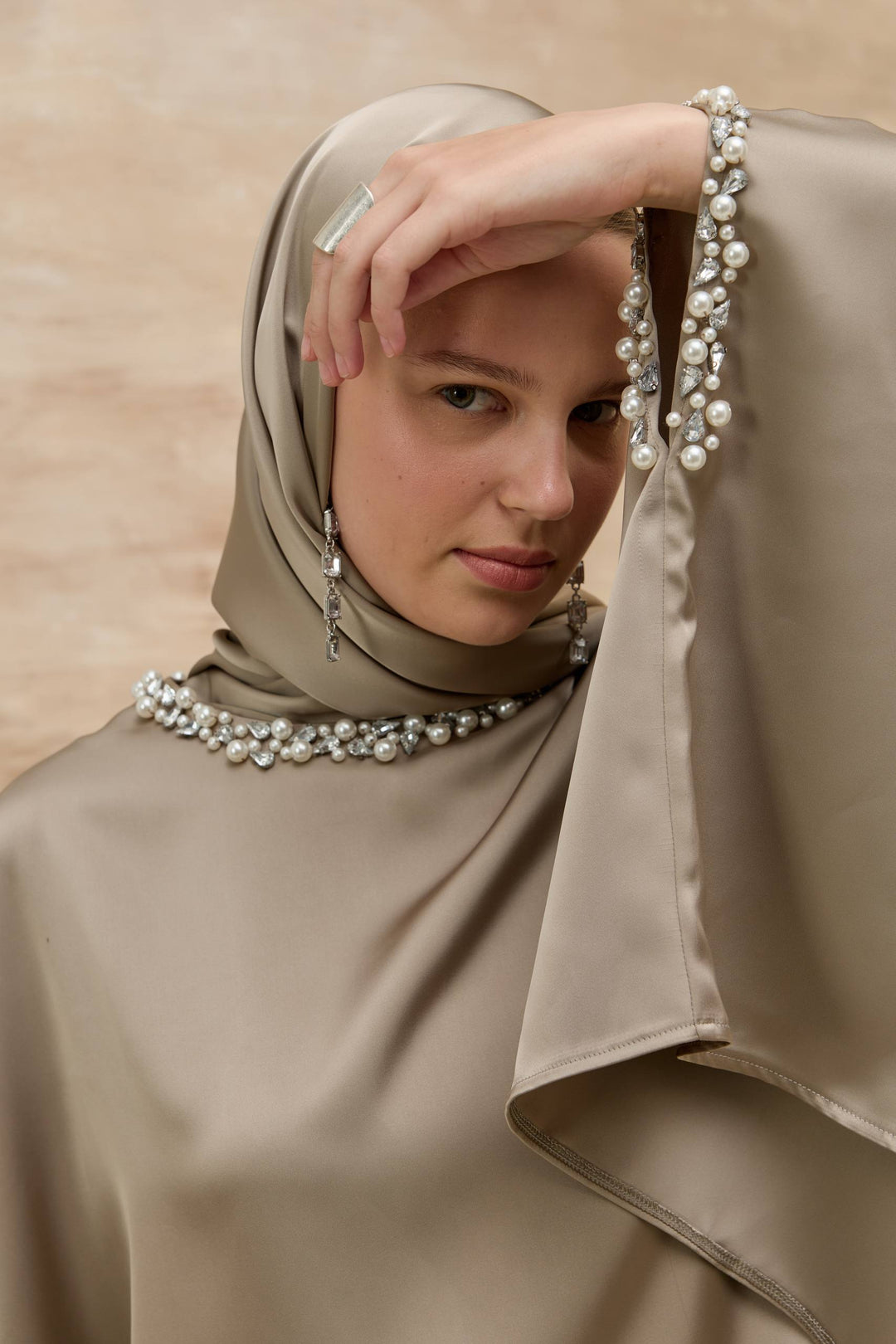 Woman wearing a beige hijab with pearl details against a beige background