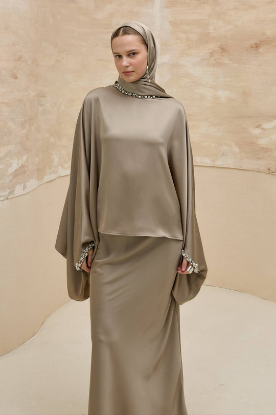 Woman wearing a beige hijab and matching outfit against a neutral background