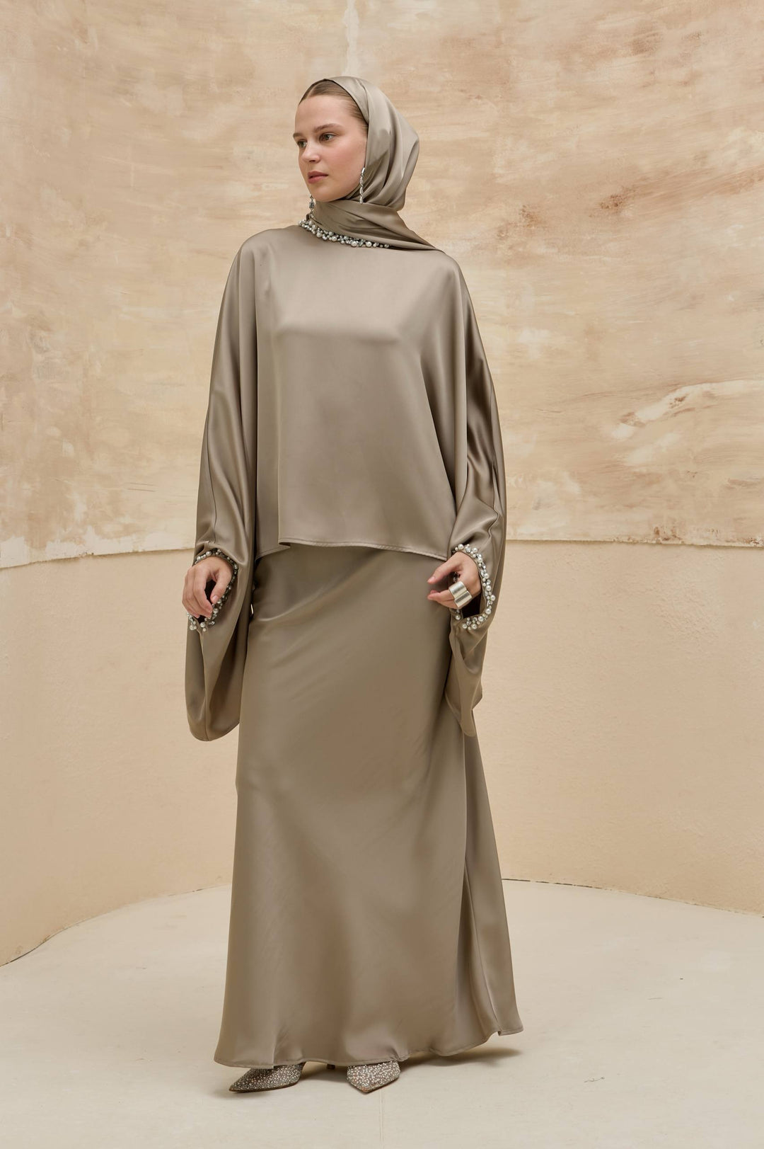 Woman wearing a beige abaya with a matching headscarf against a beige background