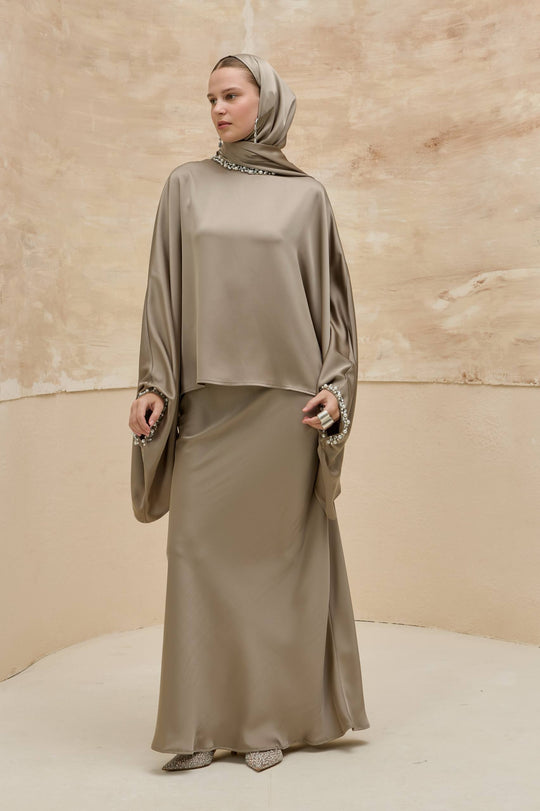 Woman wearing a beige abaya with a matching headscarf against a beige background
