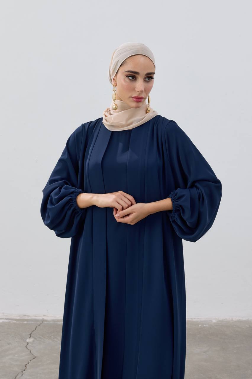 Woman wearing a navy blue abaya with a beige hijab against a white background