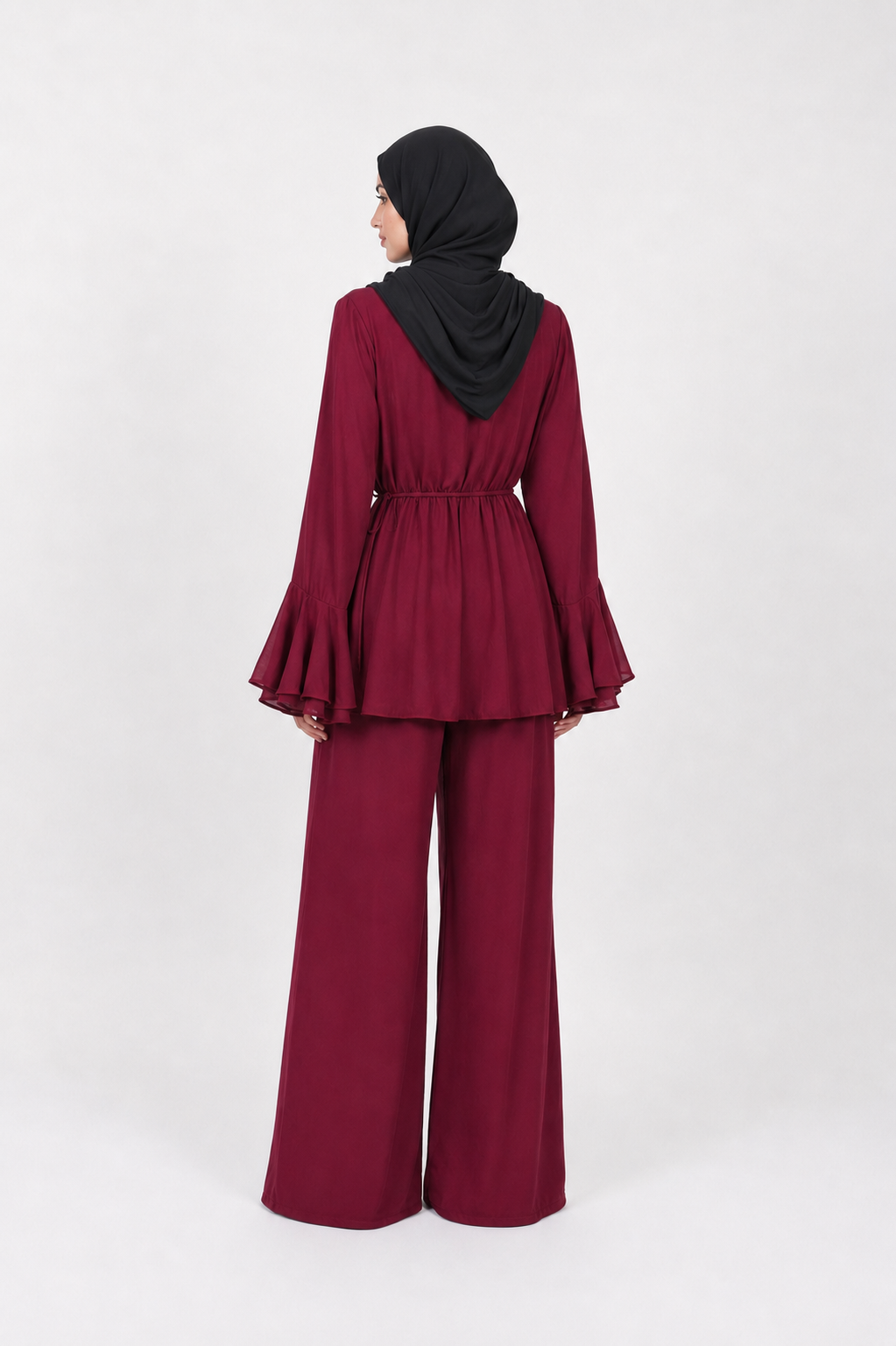 A woman wearing a matching deep burgundy two-piece outfit with wide-leg pants and a black hijab, shown from the back against a light gray studio background.