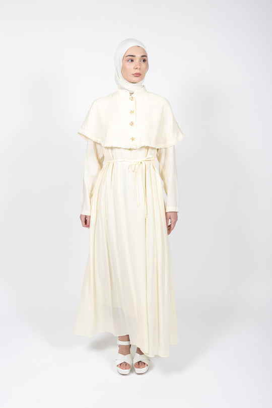Woman wearing a long, light-colored dress with a matching hijab on a white background
