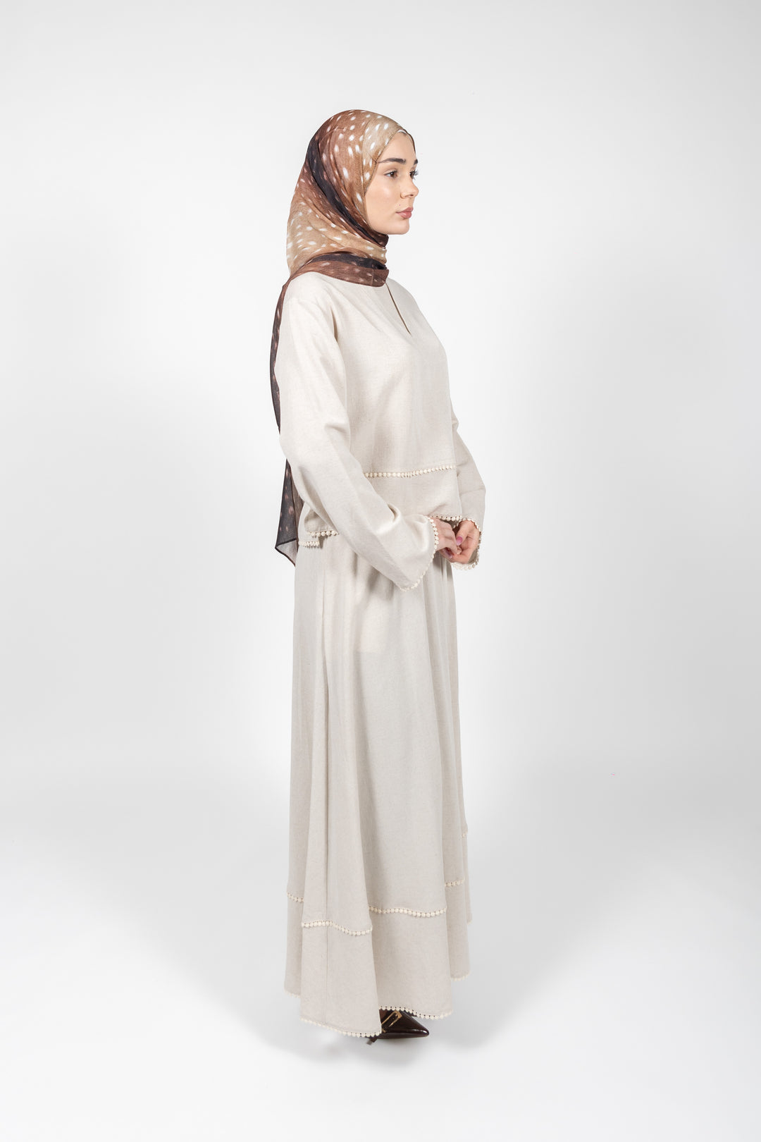 Woman wearing a long beige dress and patterned hijab on a white background