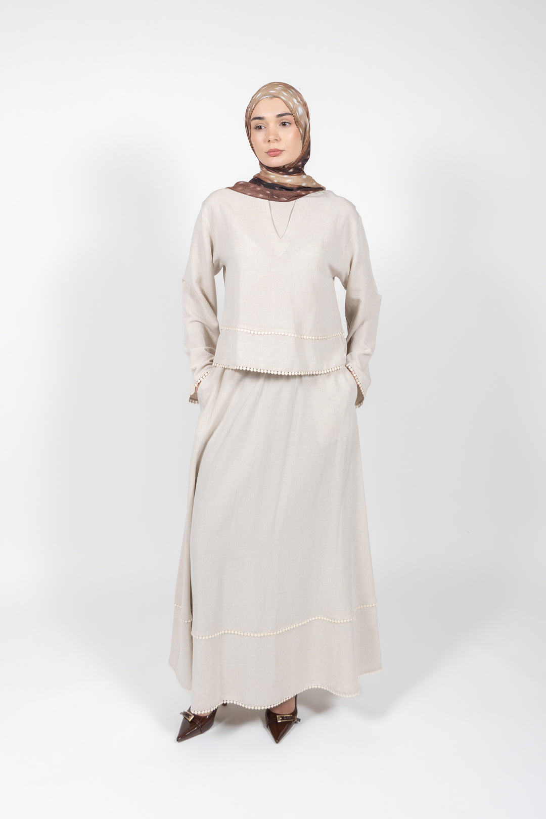 Woman wearing a beige outfit with a hijab on a white background