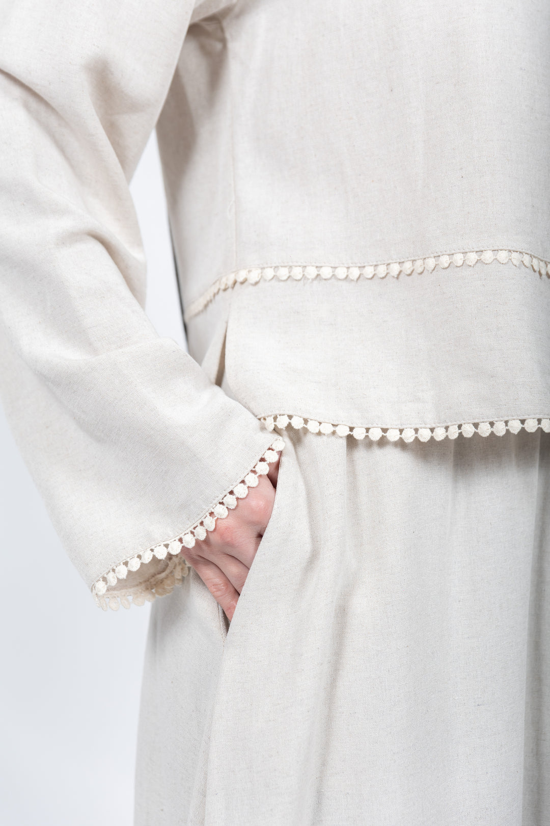 Close-up of a white garment with pearl trim on a plain background