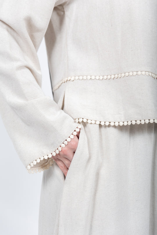 Close-up of a white garment with pearl trim on a plain background
