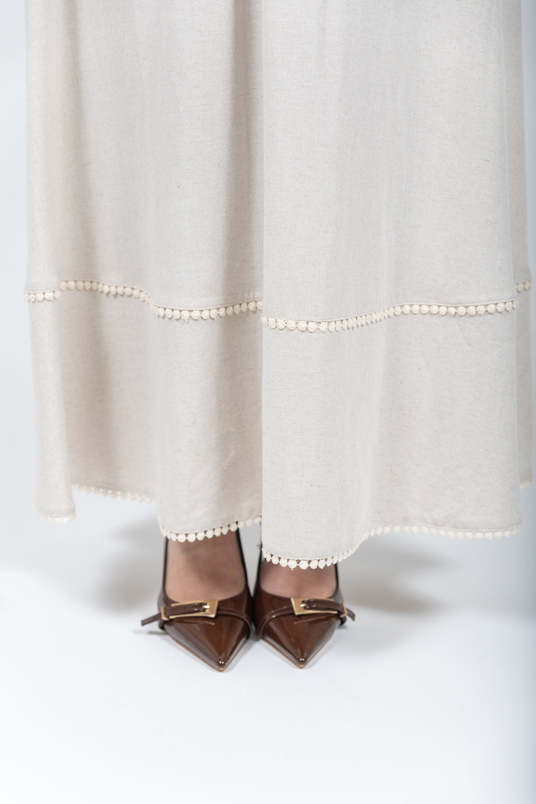 Brown pointed-toe shoes with decorative bows worn with a white dress, accentuated by a string of pearls.