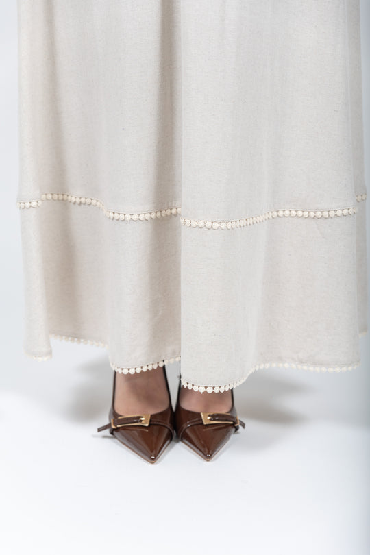 Brown pointed-toe shoes with decorative bows worn with a white dress, accentuated by a string of pearls.