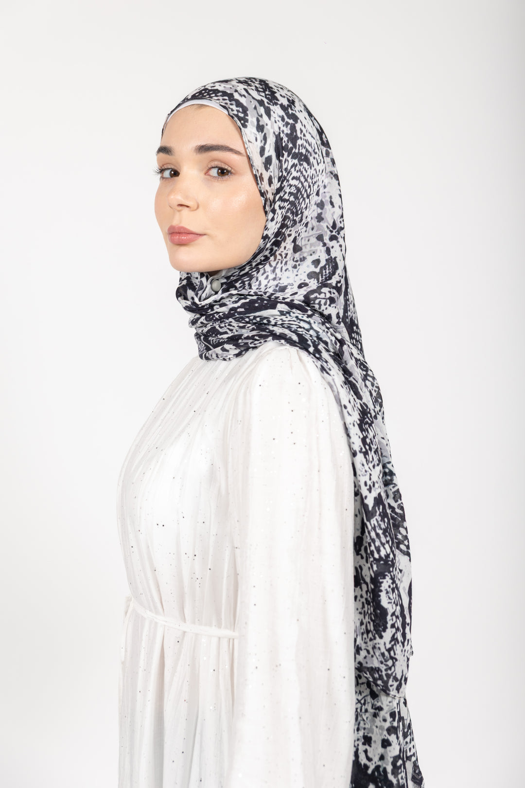 Woman wearing a patterned hijab and white dress on a white background