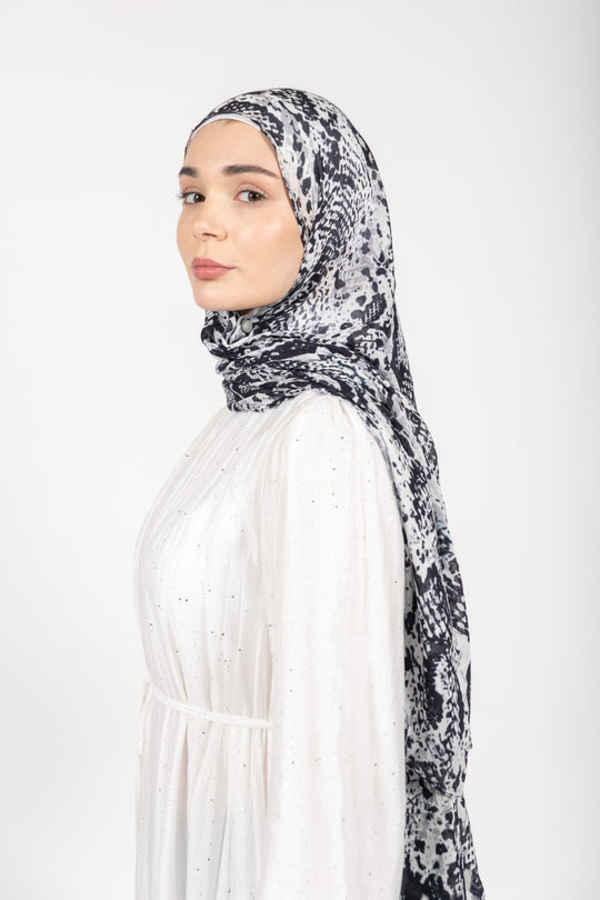 Woman wearing a patterned hijab and white dress on a white background