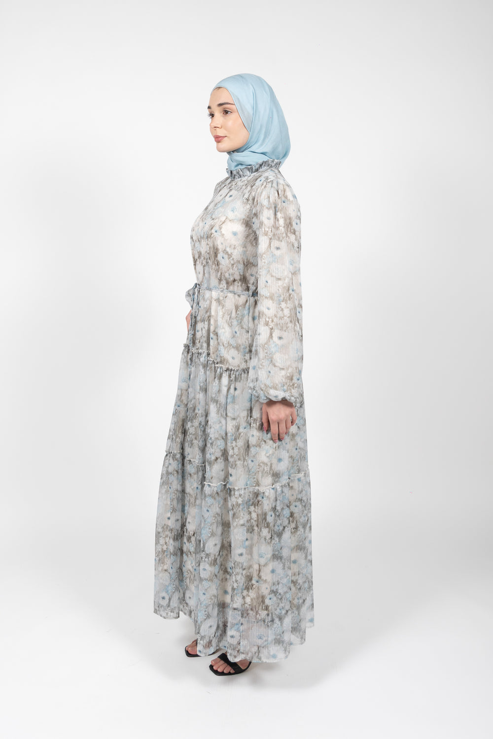 Woman wearing a long floral dress and light blue hijab on a white background