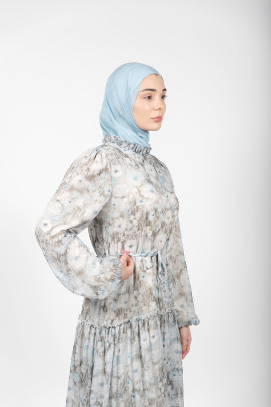 Woman wearing a floral dress and light blue hijab on a white background