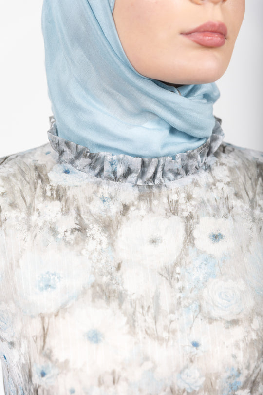 Person wearing a light blue hijab and a floral dress with white and blue patterns.