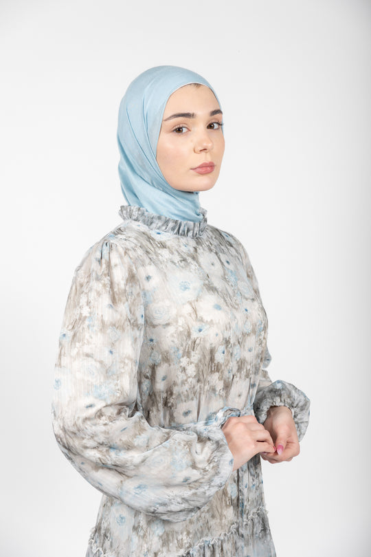 Woman wearing a light blue hijab and a patterned dress on a white background