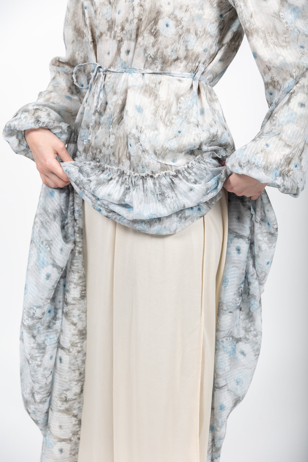 Person wearing a floral dress with a belt and beige pants on a white background
