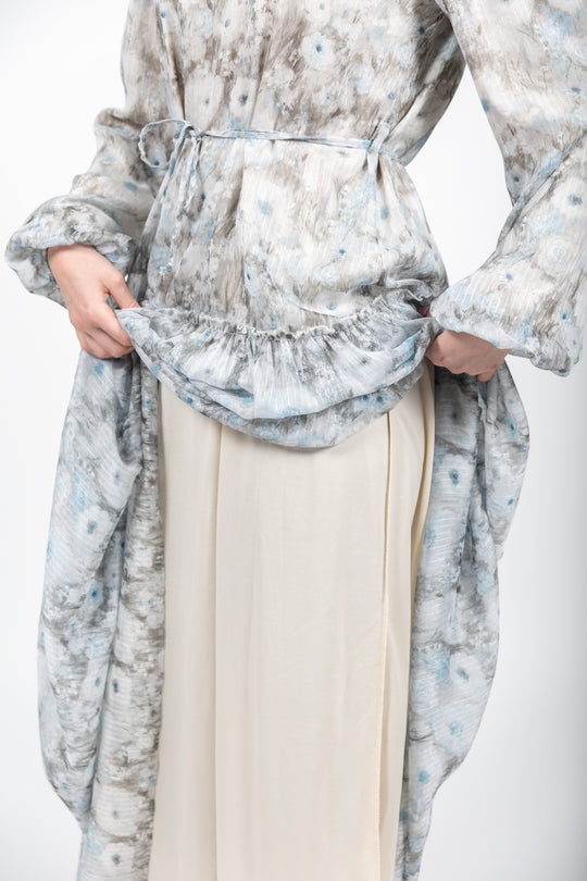 Person wearing a floral dress with a belt and beige pants on a white background