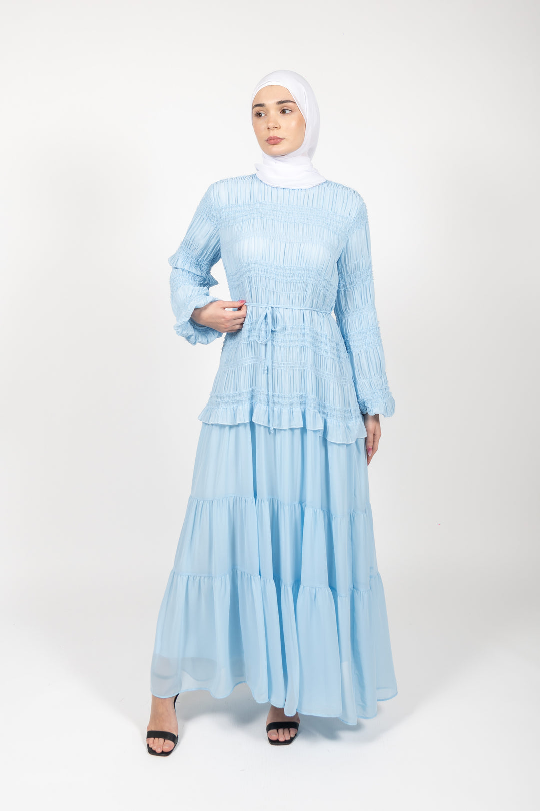 Woman wearing a light blue dress with a hijab on a white background