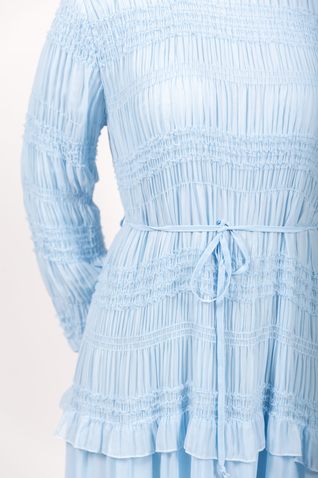 Light blue dress with smocked bodice and ruffled layers on a white background