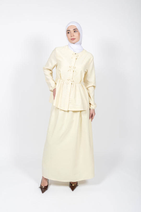 Woman wearing a light yellow outfit with a hijab on a white background