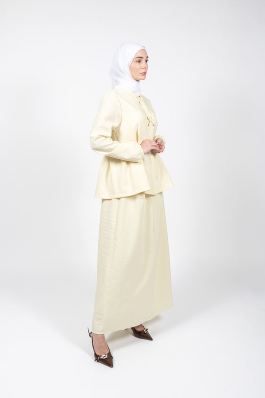 Woman wearing a light yellow outfit with a hijab on a white background