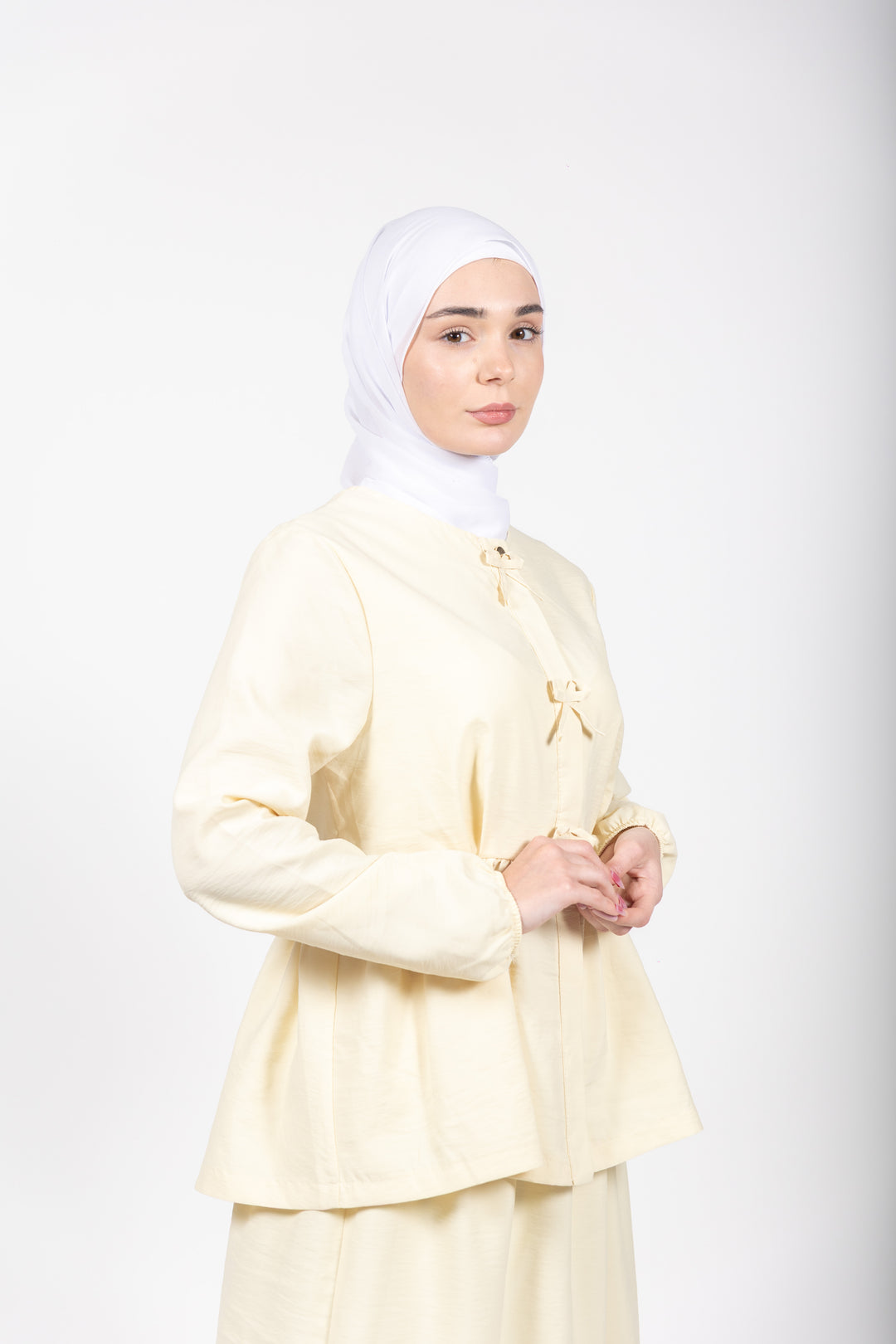Woman wearing a light yellow outfit with a hijab on a white background