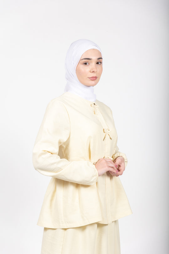 Woman wearing a light yellow outfit with a hijab on a white background