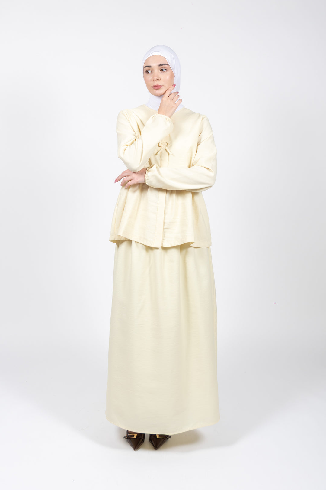 Woman wearing a cream-colored outfit with a matching hijab on a white background