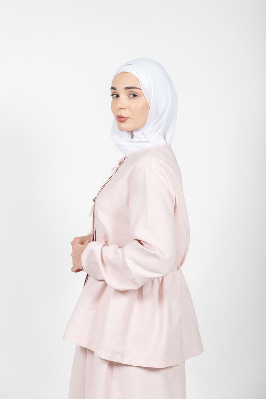 Woman wearing a light pink outfit with a hijab on a white background