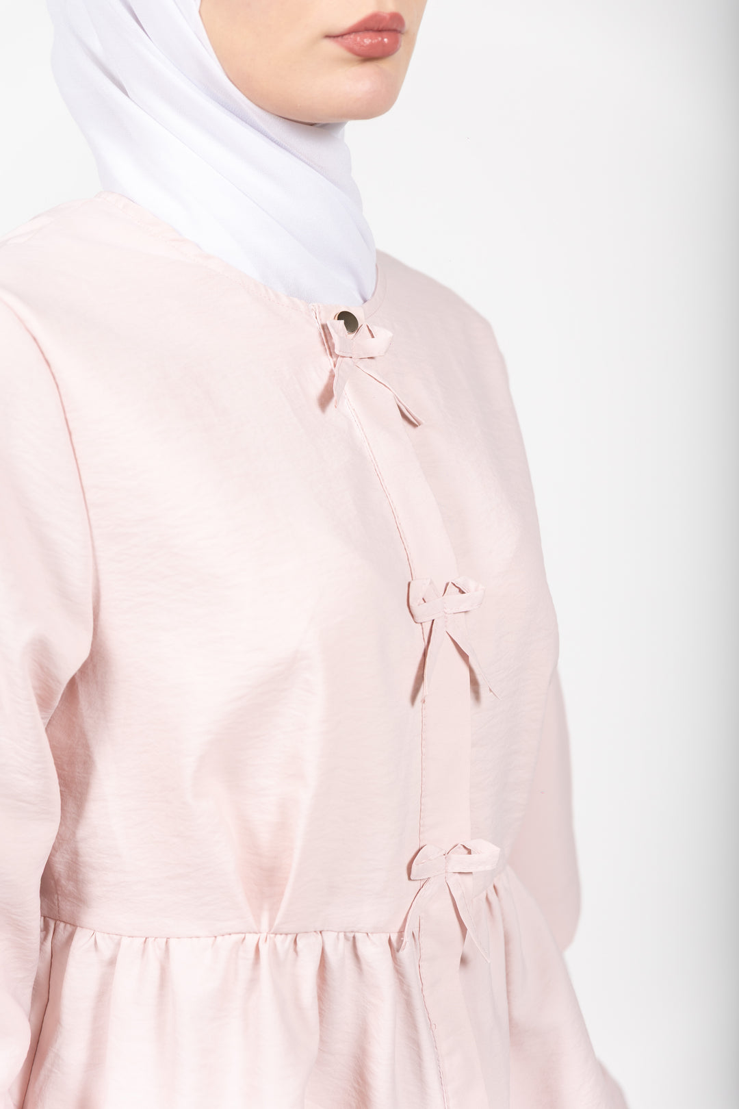 Person wearing a light pink dress with a white hijab on a plain background