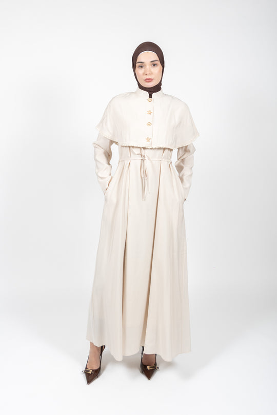 Woman wearing a long cream-colored dress with a matching hijab on a white background