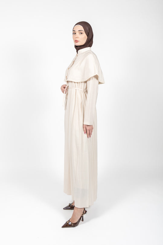 Woman wearing a long beige dress with a high collar on a white background