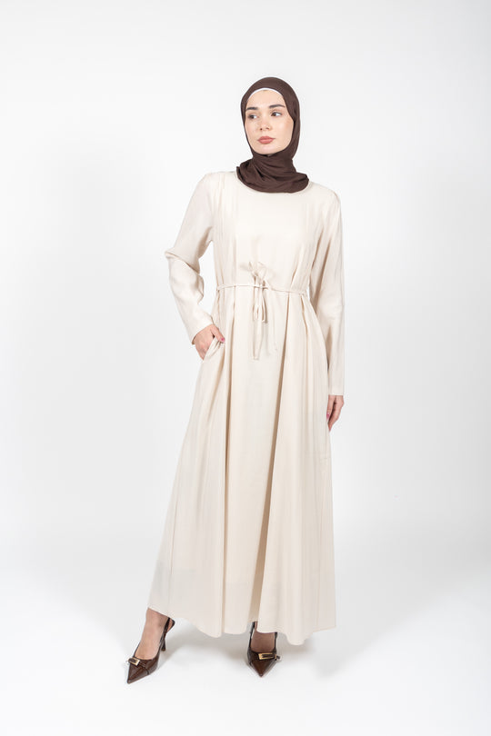 Woman wearing a long beige dress and brown hijab on a white background