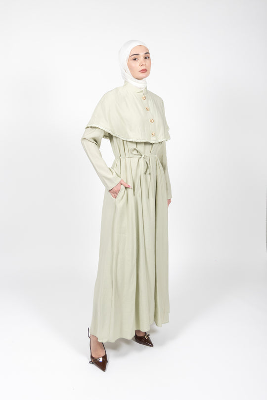 Woman wearing a light green dress with a matching hijab on a white background