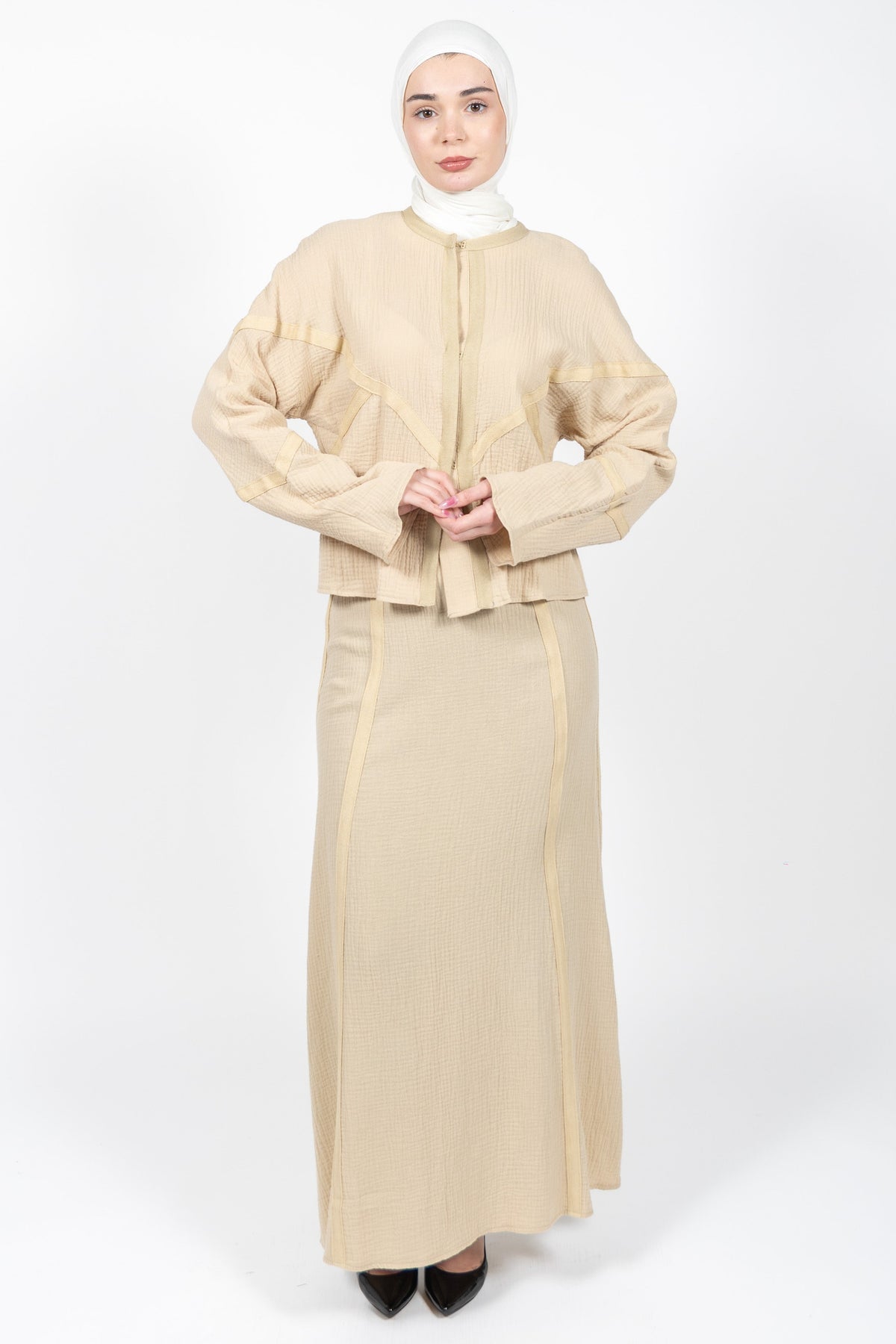 Woman wearing a beige outfit with a matching hijab on a white background