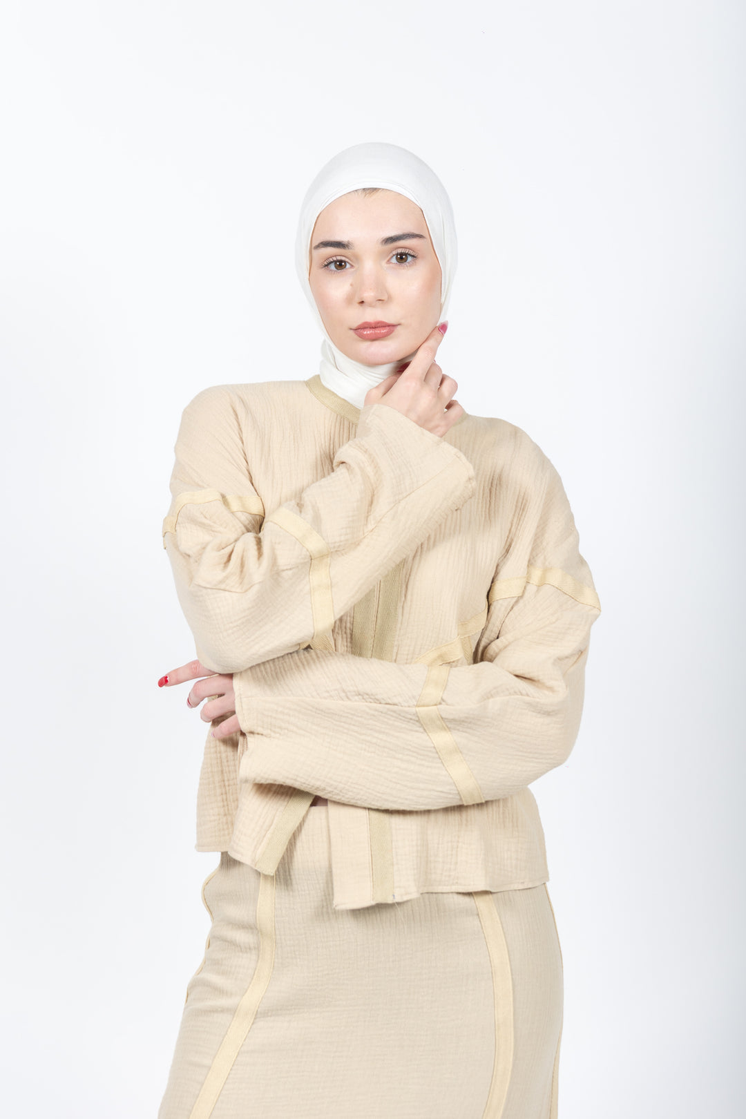 Woman wearing a beige outfit with a matching hijab on a white background