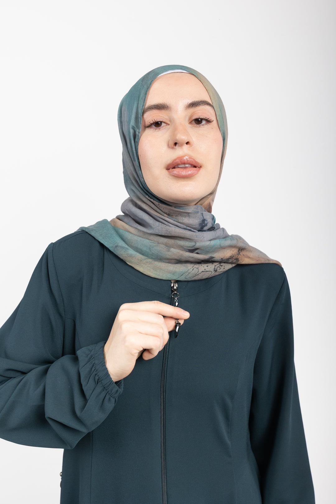 Woman wearing a dark green outfit with a patterned hijab on a white background