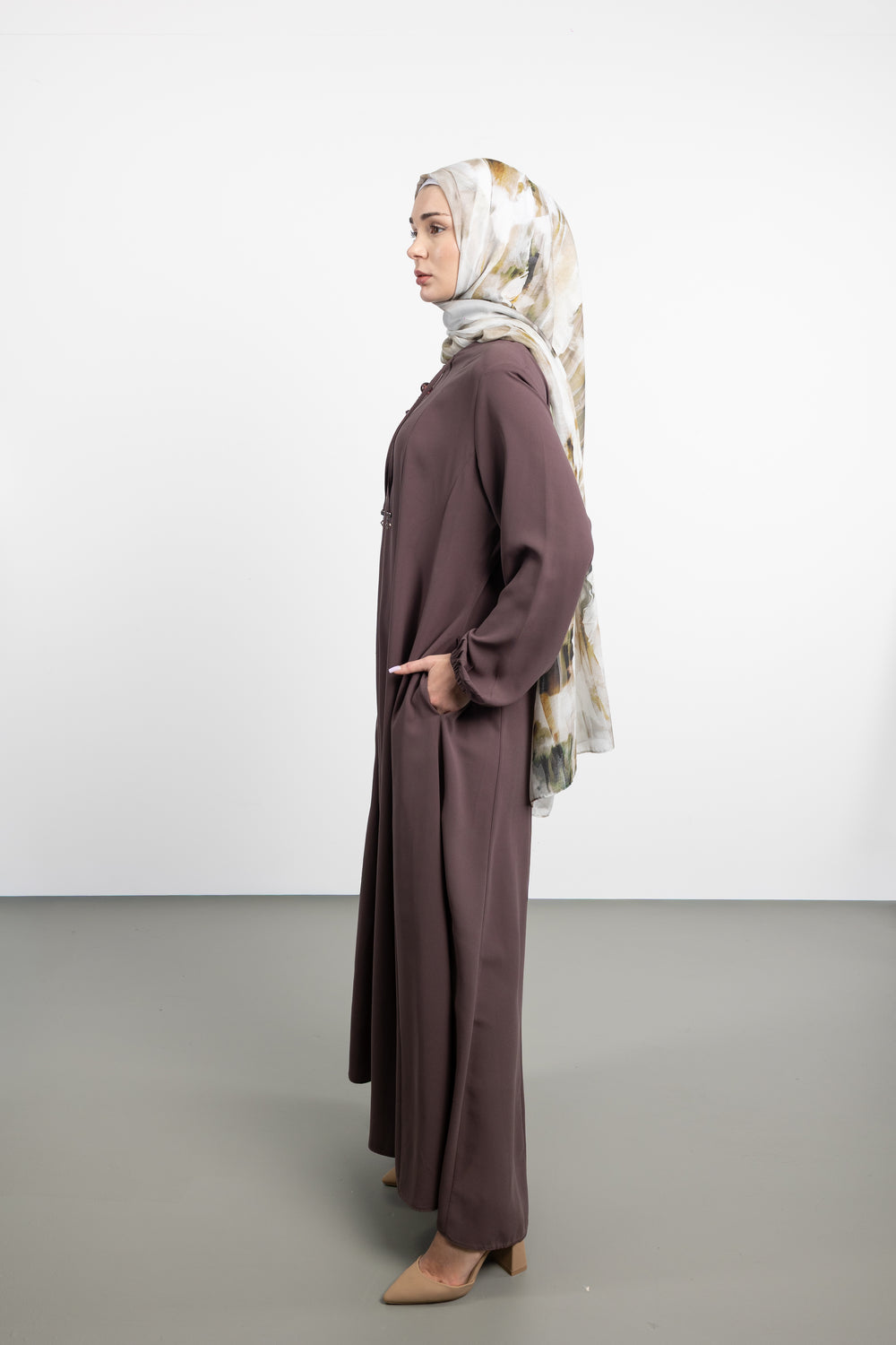 Woman wearing a long brown dress and patterned hijab on a white background