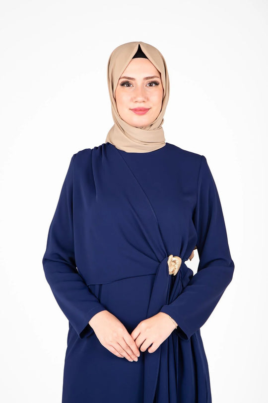 Woman wearing a navy blue dress with a beige hijab on a white background